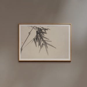 Puede incluir: Una obra de arte enmarcada con una pintura minimalista a la tinta de bamb&uacute;. La obra muestra una rama con hojas de color gris oscuro y un tallo delgado sobre un fondo beige claro. El marco es de color marr&oacute;n claro.
