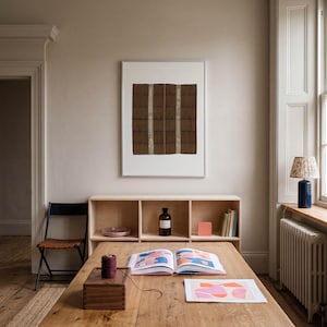 Brown vintage textile print in a white frame above a wooden desk. Woven pattern wall art for home office decor, creative studios, Scandinavian interiors, and neutral living spaces.