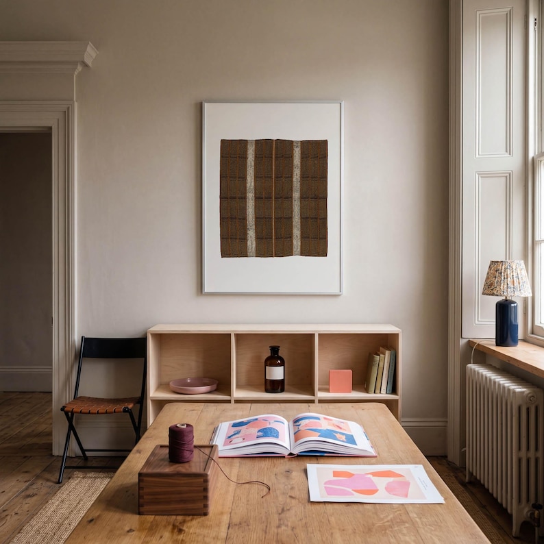 Brown vintage textile print in a white frame above a wooden desk. Woven pattern wall art for home office decor, creative studios, Scandinavian interiors, and neutral living spaces.