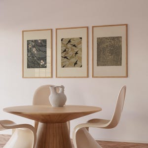 Gallery wall set of three framed Japanese art prints featuring floral blossoms, nature-inspired patterns, and botanical details, displayed above a round wooden dining table in a warm neutral dining room.