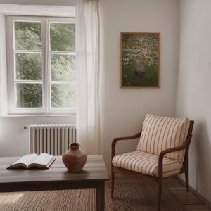 Op de afbeelding: Een gestreepte fauteuil met een houten frame staat in een kamer met een raam, een terracotta vaas en een boek op een houten tafel. Een ingelijst afdruk van een schilderij met twee figuren in een bloemenveld hangt aan de muur.