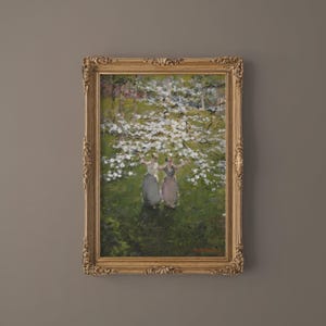 Op de afbeelding: Een ingelijst olieverfschilderij dat drie vrouwen in lange jurken toont die onder een bloeiende boom staan. Het schilderij is gesitueerd in een weelderig groen landschap met een zachte, impressionistische stijl.