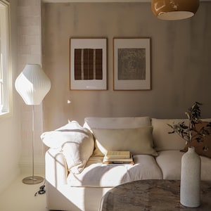 Set of 2 vintage framed prints styled above a cream linen sofa, featuring warm neutral tones, sculptural lighting and organic modern living room decor