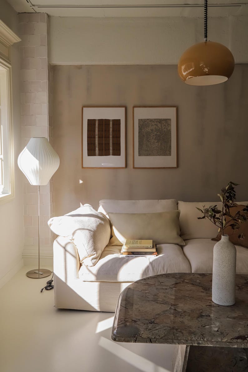 Set of 2 vintage framed prints styled above a cream linen sofa, featuring warm neutral tones, sculptural lighting and organic modern living room decor