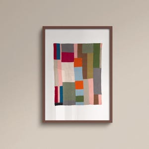 May include: A framed textile artwork with a patchwork design. The quilt features rectangular and square patches in various colours, including pink, green, orange, and grey. The artwork is displayed in a brown frame.