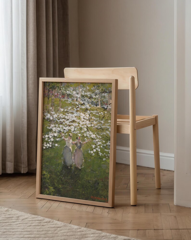 Op de afbeelding: Een ingelijst schilderij van drie vrouwen die in een veld met witte bloemen staan. Het schilderij is in een licht houten lijst en hangt aan een muur.