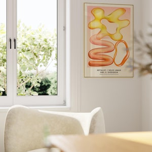 Puede incluir: Una impresi&oacute;n art&iacute;stica enmarcada con formas abstractas en tonos amarillo, naranja y rosa. La obra, titulada "Metallic / Solid Liquid" de Emil U. Sverisson, se exhibe en un marco dorado. La impresi&oacute;n cuelga de una pared blanca, cerca de una ventana y una silla color crema.