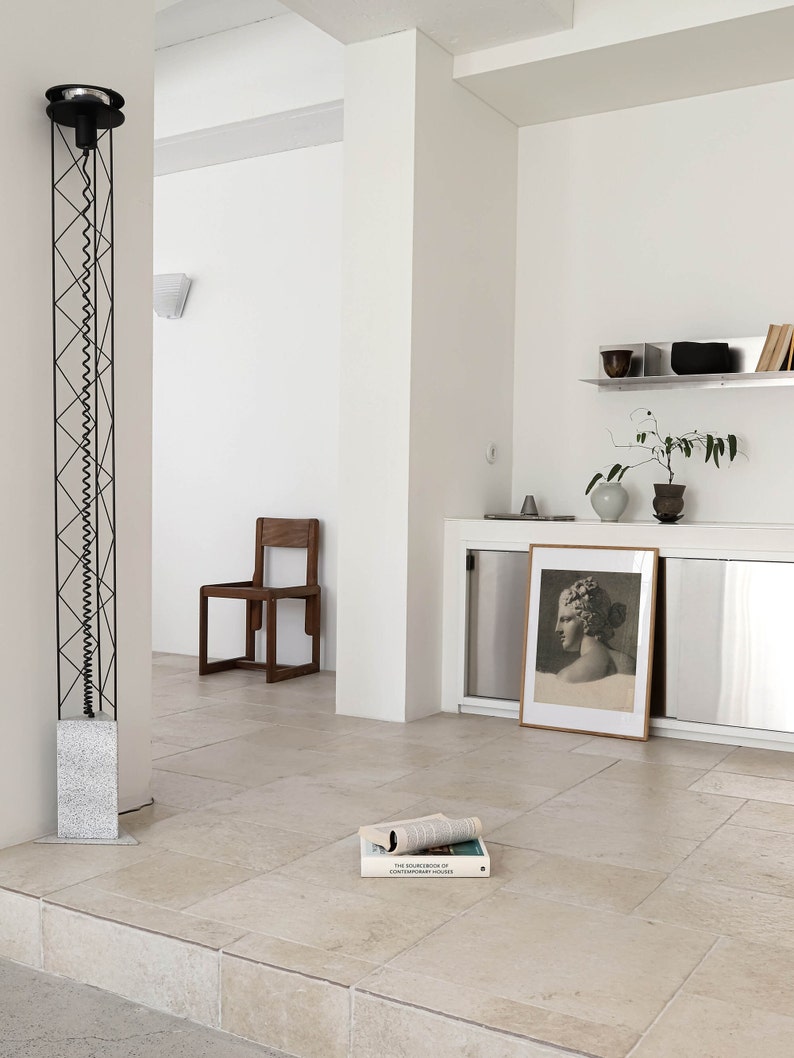 May include: A white room with a black floor lamp, a wooden chair, a framed print, and a book titled "The Sourcebook of Contemporary Houses".