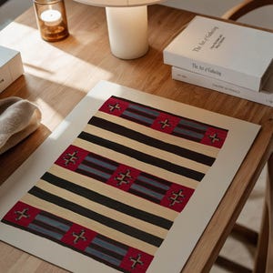 May include: A rectangular print featuring a geometric pattern with alternating black and beige stripes. Red squares with cross-like designs are interspersed throughout. The print is displayed on a wooden table, alongside books and a lamp.