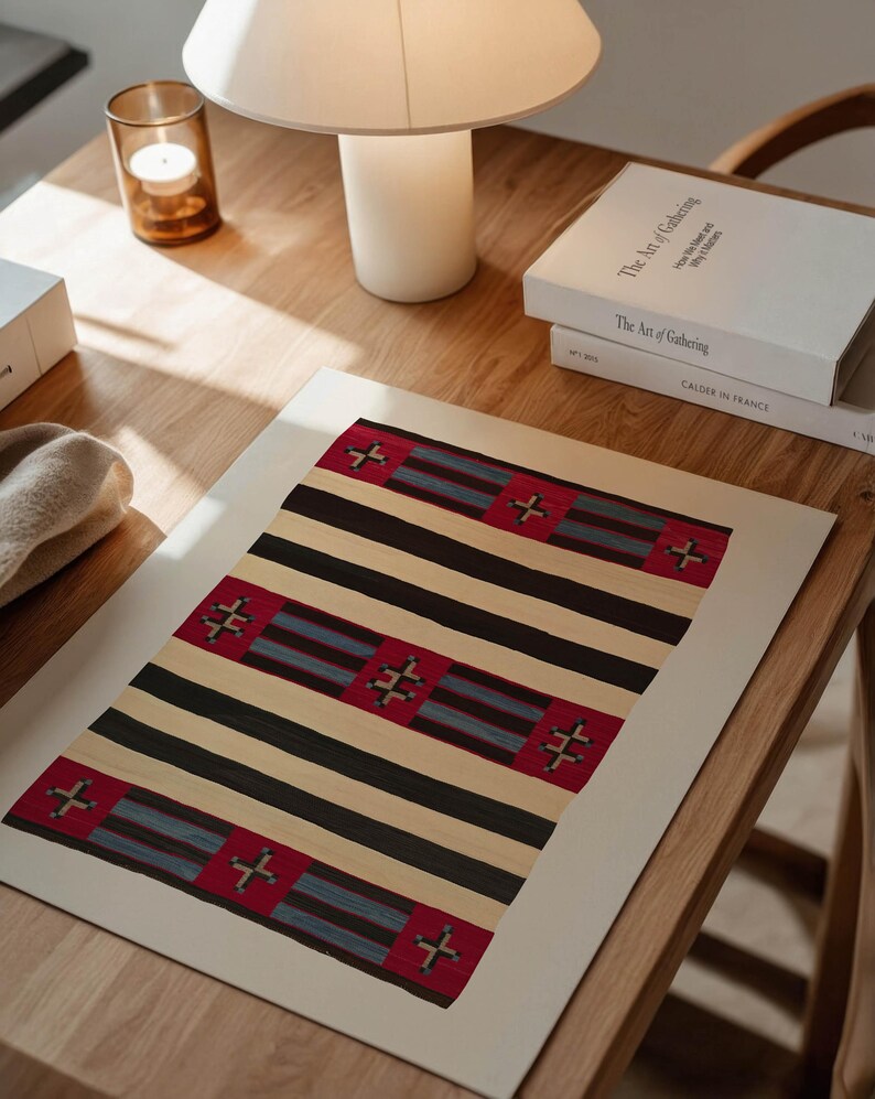 May include: A rectangular print featuring a geometric pattern with alternating black and beige stripes. Red squares with cross-like designs are interspersed throughout. The print is displayed on a wooden table, alongside books and a lamp.