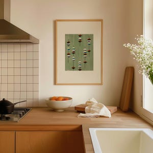 May include: A framed print with a green background and a pattern of hanging, diamond-shaped designs in shades of brown, white, and blue. The print is displayed in a kitchen setting with a wooden countertop and a white sink.