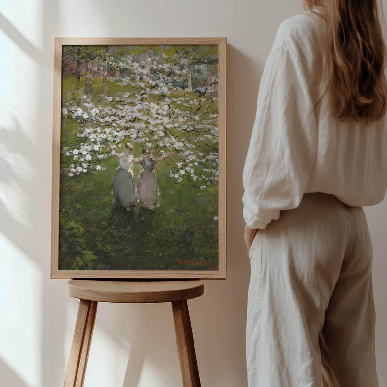 Op de afbeelding: Een ingelijst schilderij dat drie vrouwen toont die in een veld met witte bloemen staan. De vrouwen dragen lange jurken en houden elkaar vast. Het schilderij is geschilderd tegen een achtergrond van groene bomen en een blauwe lucht.