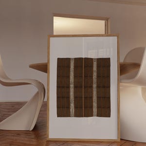 Large framed textile print leaning on the floor beside a dining table. Vintage woven pattern wall art for modern dining rooms, warm neutral interiors, and organic modern decor.
