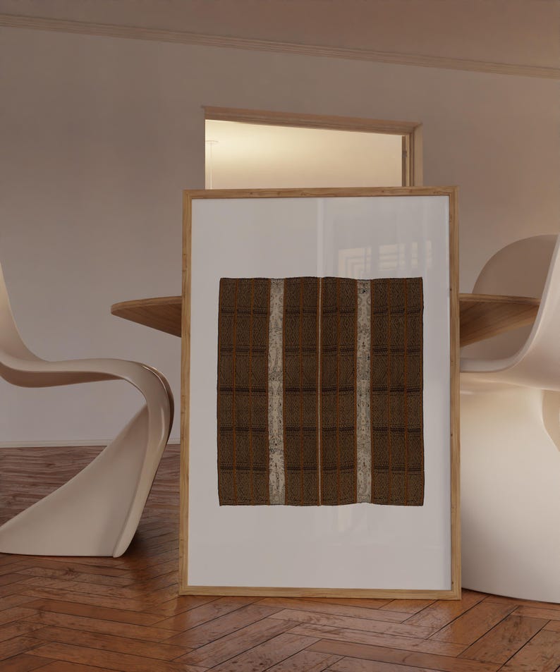Large framed textile print leaning on the floor beside a dining table. Vintage woven pattern wall art for modern dining rooms, warm neutral interiors, and organic modern decor.