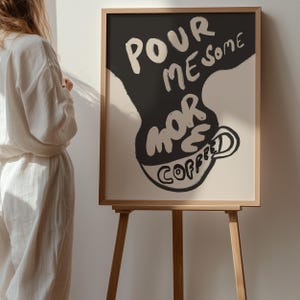 May include: A framed art print with a black and white illustration of a coffee cup with the text "Pour me some more coffee" on a white background.