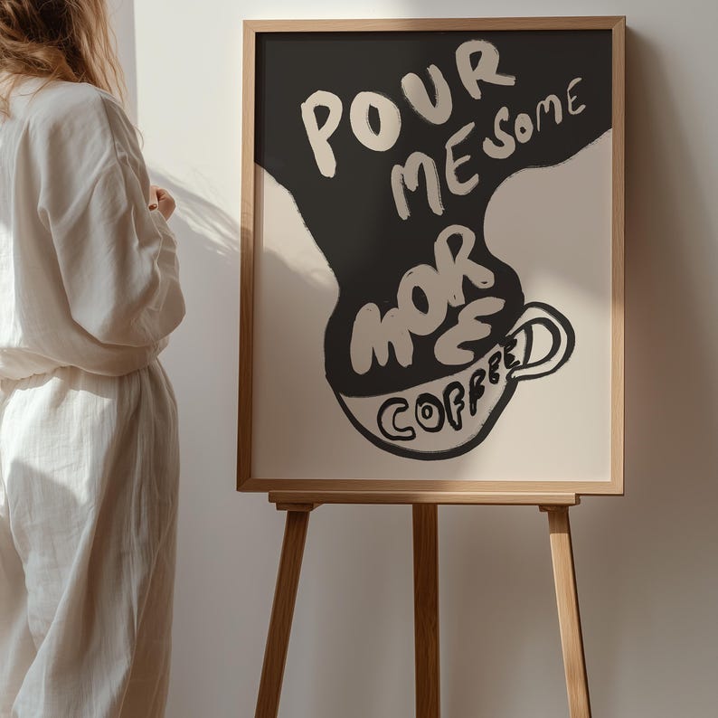 May include: A framed art print with a black and white illustration of a coffee cup with the text "Pour me some more coffee" on a white background.