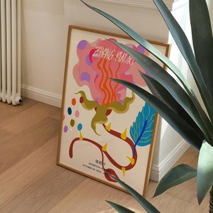 May include: A framed poster with a colorful abstract design featuring a pink, orange, and yellow flower with blue and green accents. The poster has the text "ZHANG KUOXI" and "EXHIBITION IN PROGRESS" with the dates "OCTOBER 20, 2023 - JUNE 2024".