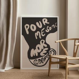 May include: A black and white framed print with the text "POUR ME SOME MORE COFFEE" in a stylized font. The print is hanging on a wall with a light brown background.