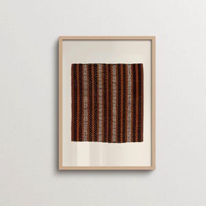 May include: A rectangular textile piece featuring vertical stripes in shades of dark brown, rust orange, and cream. The fabric displays a repeating pattern of intricate geometric motifs and small dots, all encased within a light-colored wooden frame.