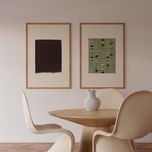 May include: Two framed abstract art prints with wooden frames. One print features a dark brown rectangular shape, and the other has a green background with a pattern of hanging shapes. A round wooden table and three cream-colored chairs are in the foreground.