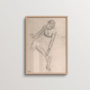 Vintage Edgar Degas ballet drawing print in a natural oak frame depicting a seated ballerina adjusting her shoe. Minimalist pencil sketch wall art with neutral tones for Japandi, Scandinavian, French country, gallery walls, and elegant home interiors.