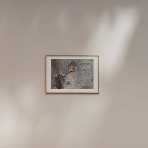 May include: A framed painting of a woman in a white dress, looking at a mirror. The painting is in a light wood frame and is set against a white wall.