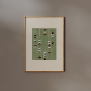May include: Abstract art print in a gold frame. The artwork features a repeating pattern of colorful, stylized shapes in shades of red, white, blue, and black against a green background. The print is displayed on a neutral-colored wall.