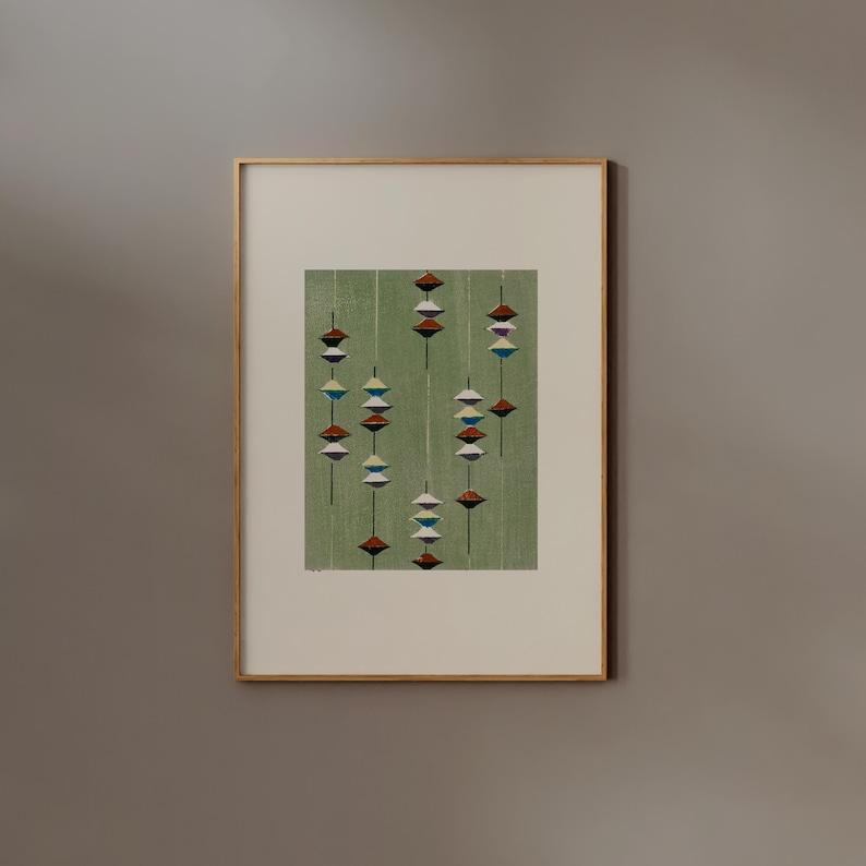 May include: Abstract art print in a gold frame. The artwork features a repeating pattern of colorful, stylized shapes in shades of red, white, blue, and black against a green background. The print is displayed on a neutral-colored wall.