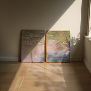 Leaning art prints in natural wood frames displayed on the floor of a sunlit neutral interior, featuring soft blue, blush and muted green pond scenery. A large art pair for floor styling, serene home decor, light wood interiors and relaxed contemporary spaces.