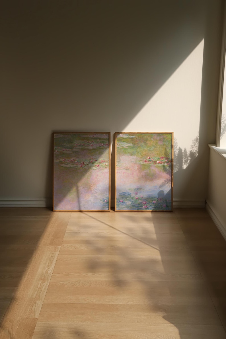 Leaning art prints in natural wood frames displayed on the floor of a sunlit neutral interior, featuring soft blue, blush and muted green pond scenery. A large art pair for floor styling, serene home decor, light wood interiors and relaxed contemporary spaces.