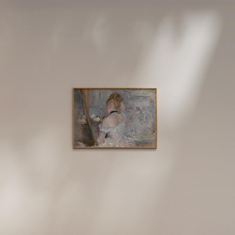 May include: A painting of a woman in a white dress, sitting in front of a mirror, with her hair up. The painting is in a gold frame and is hanging on a white wall.