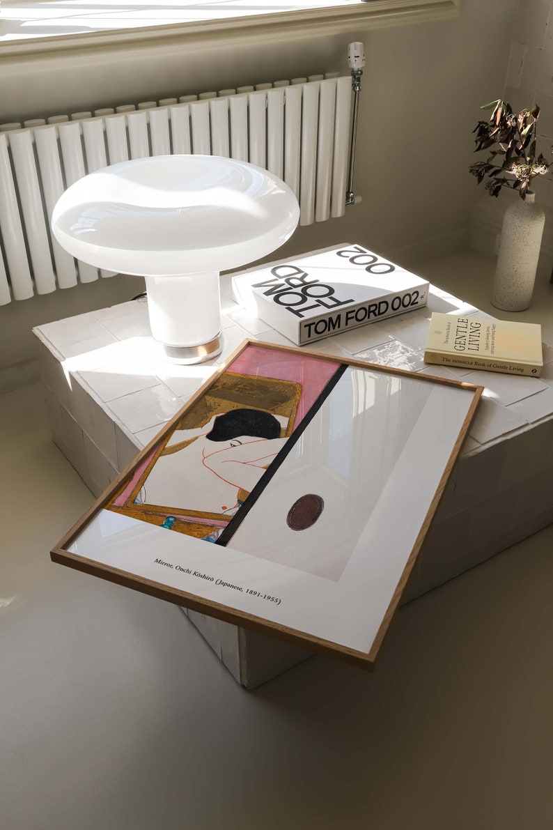 May include: A framed print of a painting by Japanese artist, Mir&oacute; Onchi Koshiro (Japanese, 1891-1955), depicts a nude figure in a pink and gold setting. The print is on a white table with a white lamp and two books, one titled "TOM FORD 002" and the other titled "GENTLE LIVING".