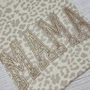 May include: A beige sweatshirt with a leopard print pattern and the word "MAMA" in gold glitter lettering.