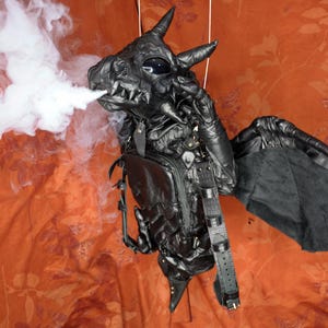 May include: A black leather dragon backpack with wings. The backpack has a zippered compartment and adjustable straps. Smoke is coming out of the dragon's mouth.