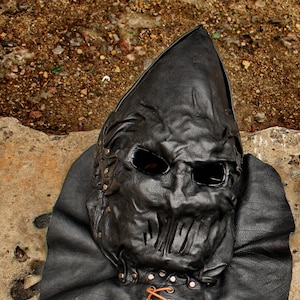 May include: A black leather mask with a pointed hood and a detailed face. The mask has a lace-up closure at the neck and is decorated with metal rivets.