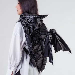 Könnte beinhalten: Ein schwarzer Lederrucksack in Form eines Drachen mit Flügeln. Der Rucksack hat ein strukturiertes, schuppiges Design und große, detaillierte Augen.