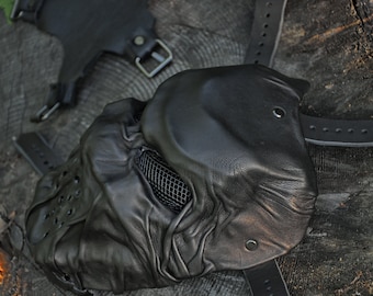 May include: A black leather mask with a mesh covering the eyes and a textured surface. The mask has a strap that goes around the head.