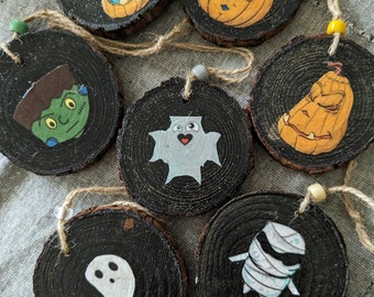 May include: Seven wooden ornaments with Halloween themes. The ornaments are painted with various characters, including a ghost, a mummy, a Frankenstein, and pumpkins. The ornaments are all round and have a rustic look.