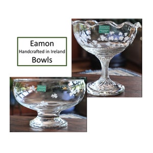 May include: Two clear glass bowls with shamrock designs. One bowl has a ruffled rim and a pedestal base. The other bowl has a rounded base. Both bowls have the text "Eamon Handcrafted in Ireland Bowls".