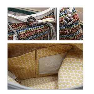 May include: A white crocheted tote bag with a colorful striped pattern and a silver heart charm. The bag has a white leather handle and a white leather lining with a yellow polka dot pattern. The lining has a leather patch with the word "Brighton" and a heart logo.