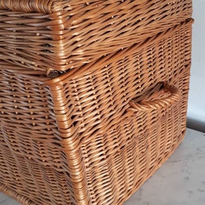 May include: A large, rectangular wicker basket with a woven handle. The basket is made of natural brown wicker and has a lid.