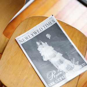 May include: A black and white newspaper with the headline "Newlywed Times" and the text "September 8, 2023" and "R&M". The newspaper features a photo of a bride and groom with the text "Ryan & Meg are getting married!"
