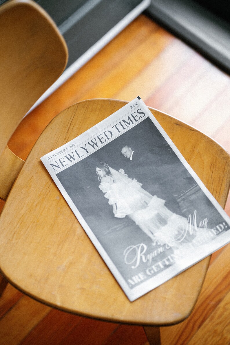 May include: A black and white newspaper with the headline "Newlywed Times" and the text "September 8, 2023" and "R&M". The newspaper features a photo of a bride and groom with the text "Ryan & Meg are getting married!"