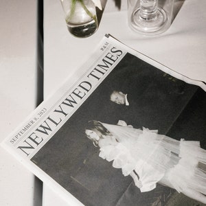 Puede incluir: Una foto en blanco y negro de una novia y un novio en la portada de un periódico titulado "Newlywed Times" con la fecha "8 de septiembre de 2023" y las iniciales "R&M" impresas en la parte superior.