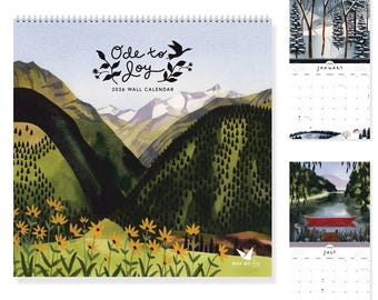 May include: A 2026 wall calendar with a spiral binding, featuring watercolor illustrations. The cover displays a mountain landscape with the text "Ode to Joy." Additional pages show seasonal scenes, including a winter forest and a summer lake with a red boat.