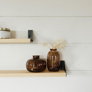 May include: Two brown glass vases with a ribbed texture, one round and one tall, on a wooden shelf with a candle and a ceramic sculpture.