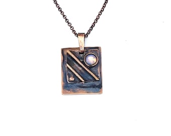 May include: A copper pendant necklace with a square-shaped pendant featuring a textured design and a small, round, iridescent stone.