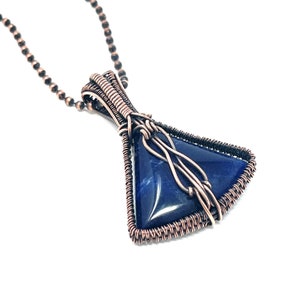 May include: A copper wire wrapped pendant featuring a triangular blue gemstone. The pendant is attached to a copper chain.