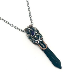 May include: A silver chain necklace with a black gemstone pendant. The pendant is wrapped in silver and copper wire and features a small amethyst gemstone.