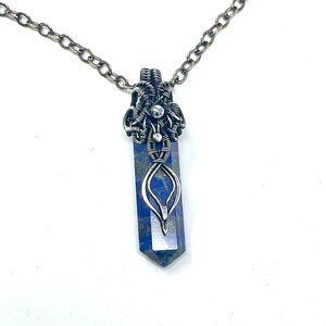 May include: A silver wire wrapped pendant featuring a blue lapis lazuli stone. The pendant is attached to a silver chain.